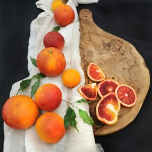 A colorful display of whole and sliced citrus fruits on a wooden board with a fabric accent.
